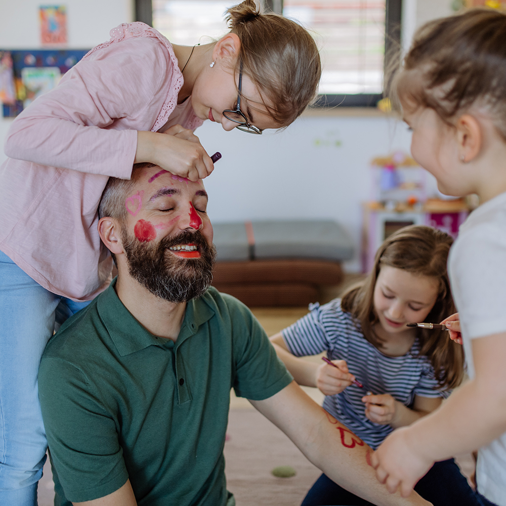three little girls putting on make up on their father